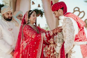Traditional Indian wedding ceremony with couple in red and cream attire exchanging vows.