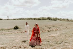 Candid shot of wedding couple in traditional dress walking through rural landscape.