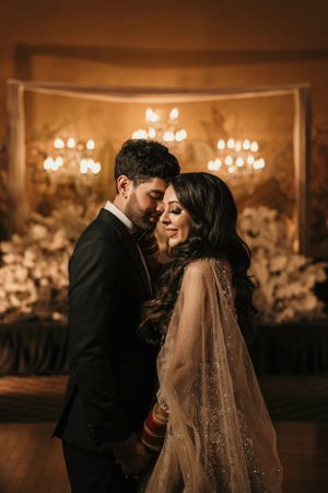 Romantic wedding portrait with warm lighting and elegant chandelier backdrop.