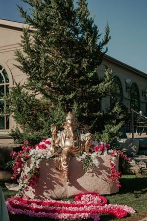 Decorative statue adorned with pink and white flowers against a building with arched windows.