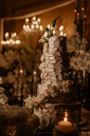 Elegant white wedding cake with cascading floral decorations illuminated by candlelight and chandeliers.