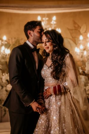 Intimate wedding moment captured in warm lighting with luxurious floral and chandelier backdrop.