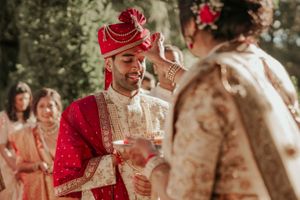 Traditional Indian wedding ceremony with participants in red and cream colored formal attire.