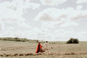 A striking red dress flows in the wind as someone stands in a serene countryside setting.