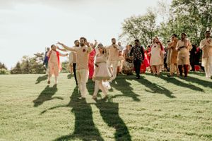 Wedding party members walking and dancing joyfully across a sunlit grassy hill.
