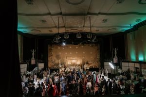 Overhead view of wedding reception with crowd dancing under chandeliers and ambient lighting.