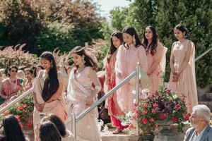 Wedding party in pastel pink attire walking down outdoor garden steps.
