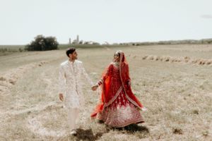 Traditional white and red wedding attire creates contrast against a rustic outdoor landscape.