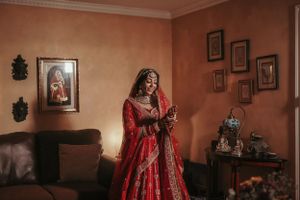 A red and gold embroidered wedding dress photographed in a traditionally decorated living room setting.