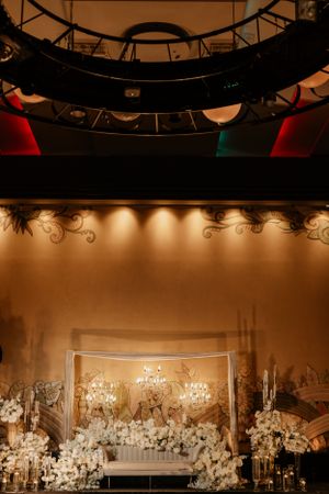 Elegant wedding venue setup with ornate chandeliers and white floral decorations against a warm-lit backdrop.