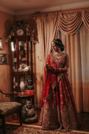 A traditional Indian bride in an ornate red lehenga poses in an elegantly decorated room.