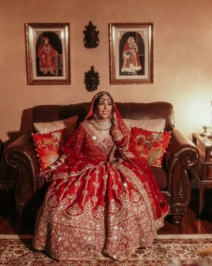 An ornate red and gold wedding lehenga being modeled on an elegant brown leather couch.