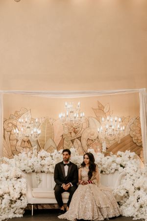 Elegant wedding backdrop featuring crystal chandeliers and white floral arrangements around a luxurious loveseat.