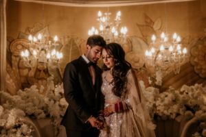 Romantic couple pose together against a backdrop of chandeliers and white flowers at their wedding.