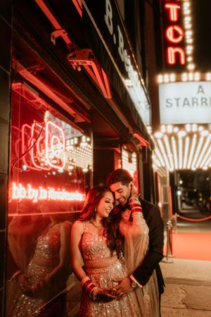 A couple poses intimately against illuminated neon signs outside a vintage theater.