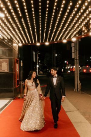 Couple walks along red carpet under theater marquee lights in elegant wedding attire.