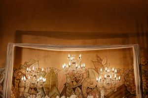 Wedding venue backdrop featuring crystal chandeliers and delicate wall murals in warm amber lighting.