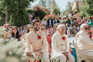 Traditional Indian wedding ceremony guests seated outdoors wearing cream and red attire on a sunny day.