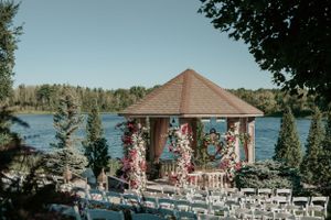 Octagonal wooden gazebo with pink floral decorations overlooking a serene lake for a wedding ceremony.