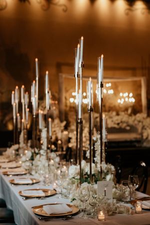 Elegant wedding reception table with tall white candles and place settings.
