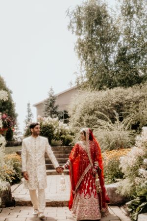 Couple in traditional Indian wedding attire walking through lush garden pathway.