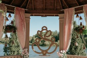 Romantic gazebo interior with pink curtains and ornate gold decorative element framing a lakeside view.