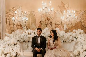 Wedding couple seated against an elegant backdrop of white flowers and crystal chandeliers.