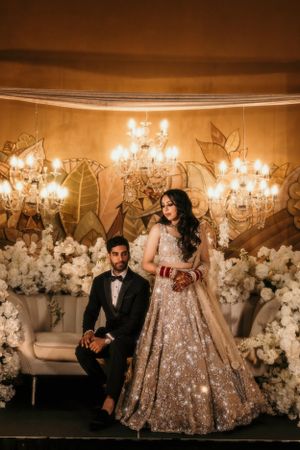 Glamorous wedding photo featuring a couple posing with ornate chandeliers and floral decorations.