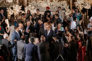 Large crowd mingling at elegant wedding reception with ornate decor and lighting.