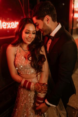 A romantic couple in formal attire sharing an intimate moment under red neon lighting.