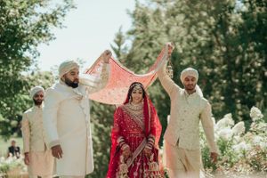 Wedding ceremony outdoors with traditional red dupatta being held over couple.