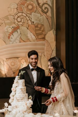 Couple cutting their wedding cake together against an ornately decorated background.