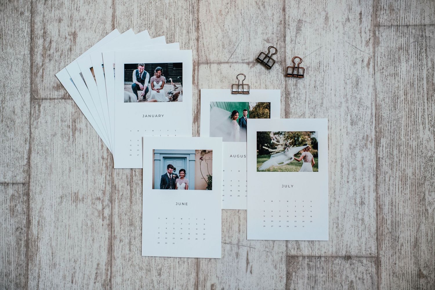 Wedding photo prints and calendar pages arranged on a rustic wooden floor.