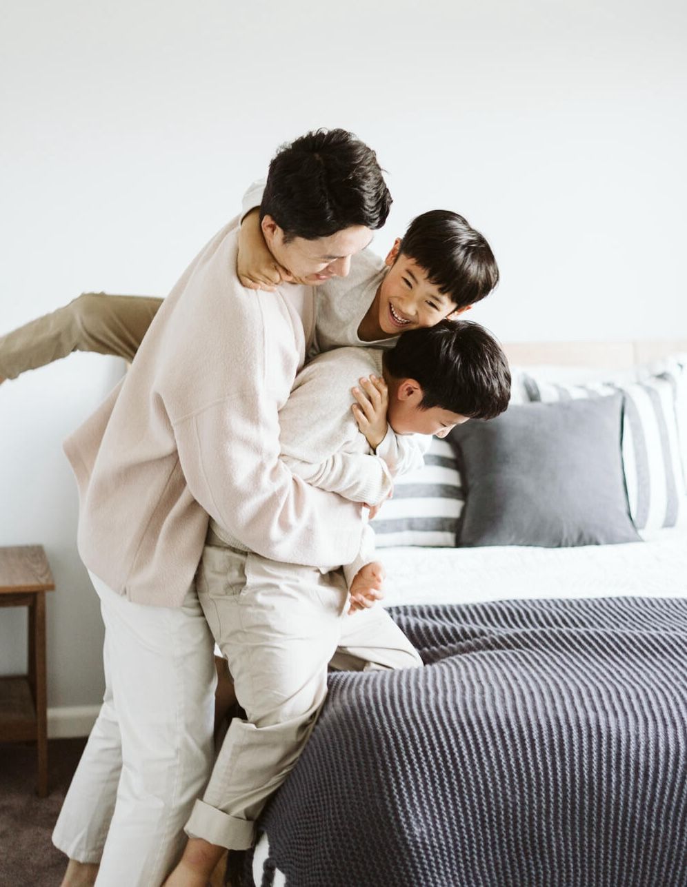 Father and two son, playing wrestling around the bed.