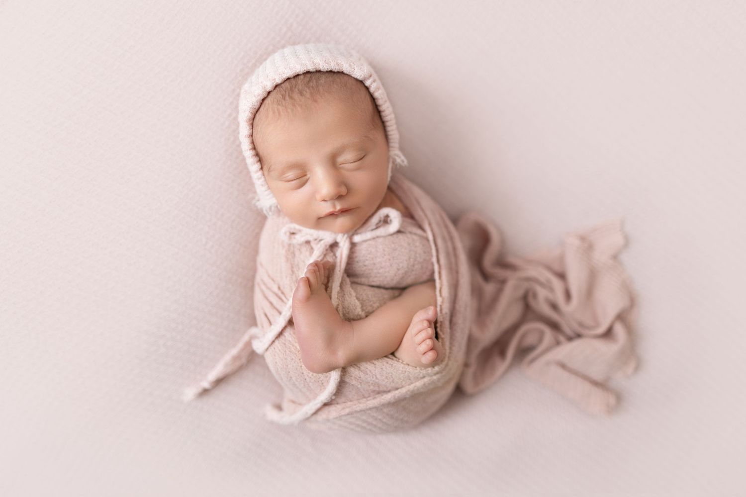 Artistic newborn portrait with baby in pink wrap against light background.