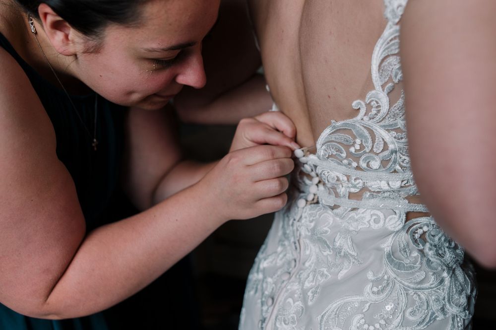 Close-up of detailed lace work being adjusted on back of white wedding dress.