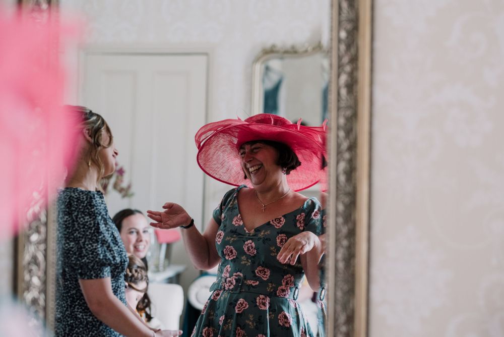 Two figures in floral dresses with one wearing a bright pink hat during a celebration.