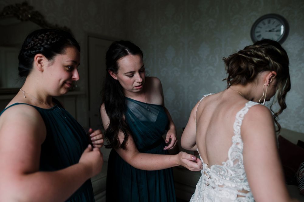 Group helping with wedding dress preparations in dimly lit room.