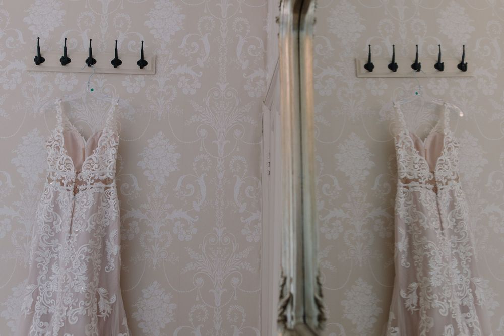 Two identical white lace wedding dresses hanging on display with black hooks against a patterned wall.
