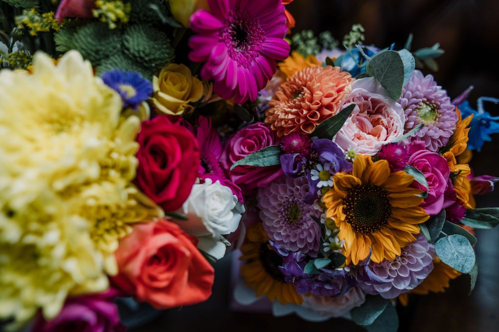 Vibrant wedding bouquet featuring sunflowers, roses, and mixed flowers in yellow, purple, and pink hues.