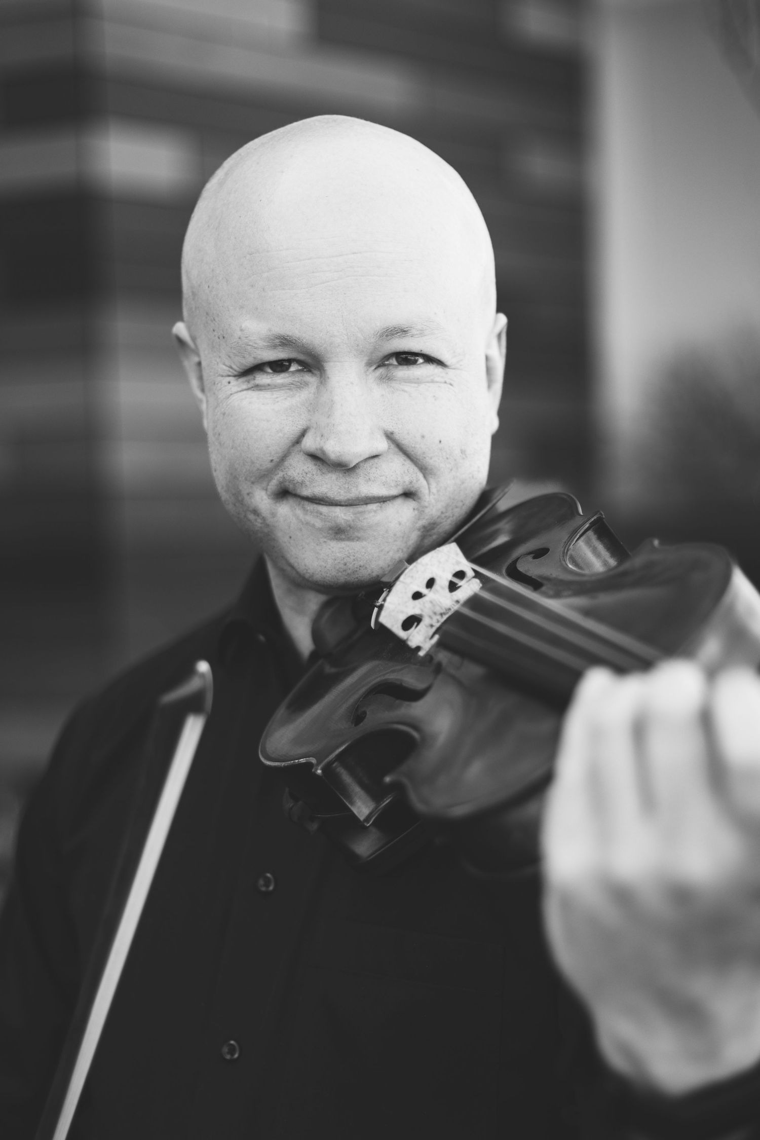 A bald musician smiling at the camera in a black and white portrait, holding a violin and bow. Musician Headshot
