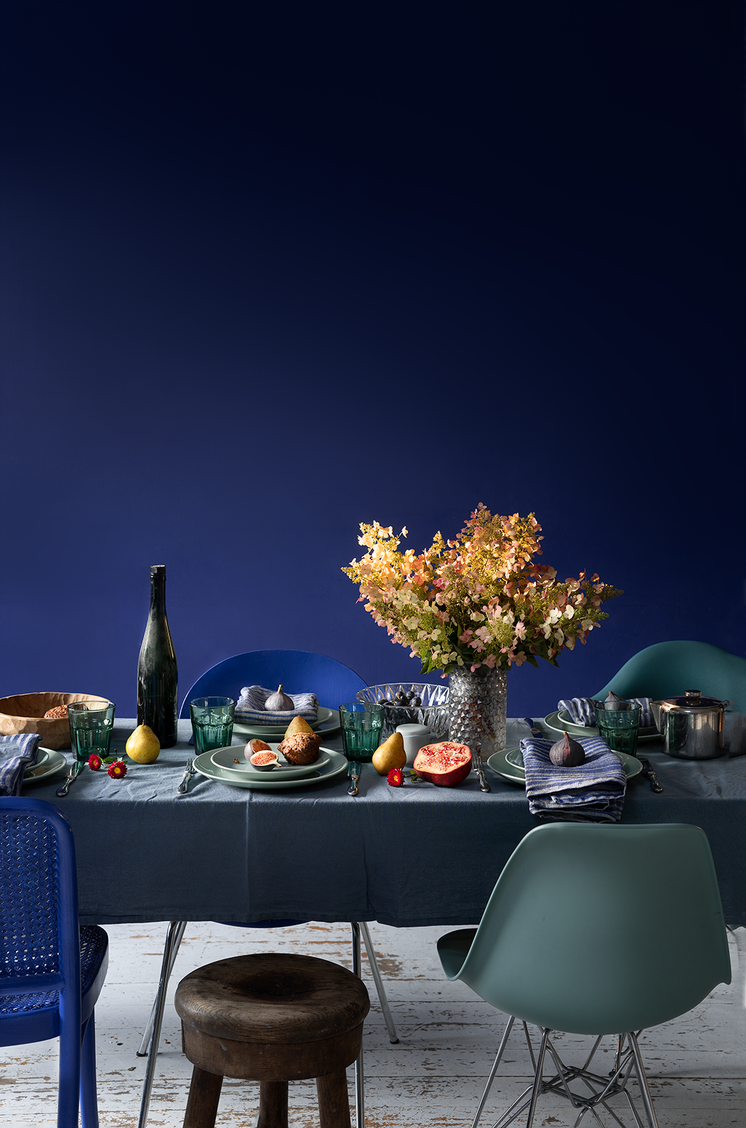Elegant table setting with autumn flowers and green chairs against deep blue background.
