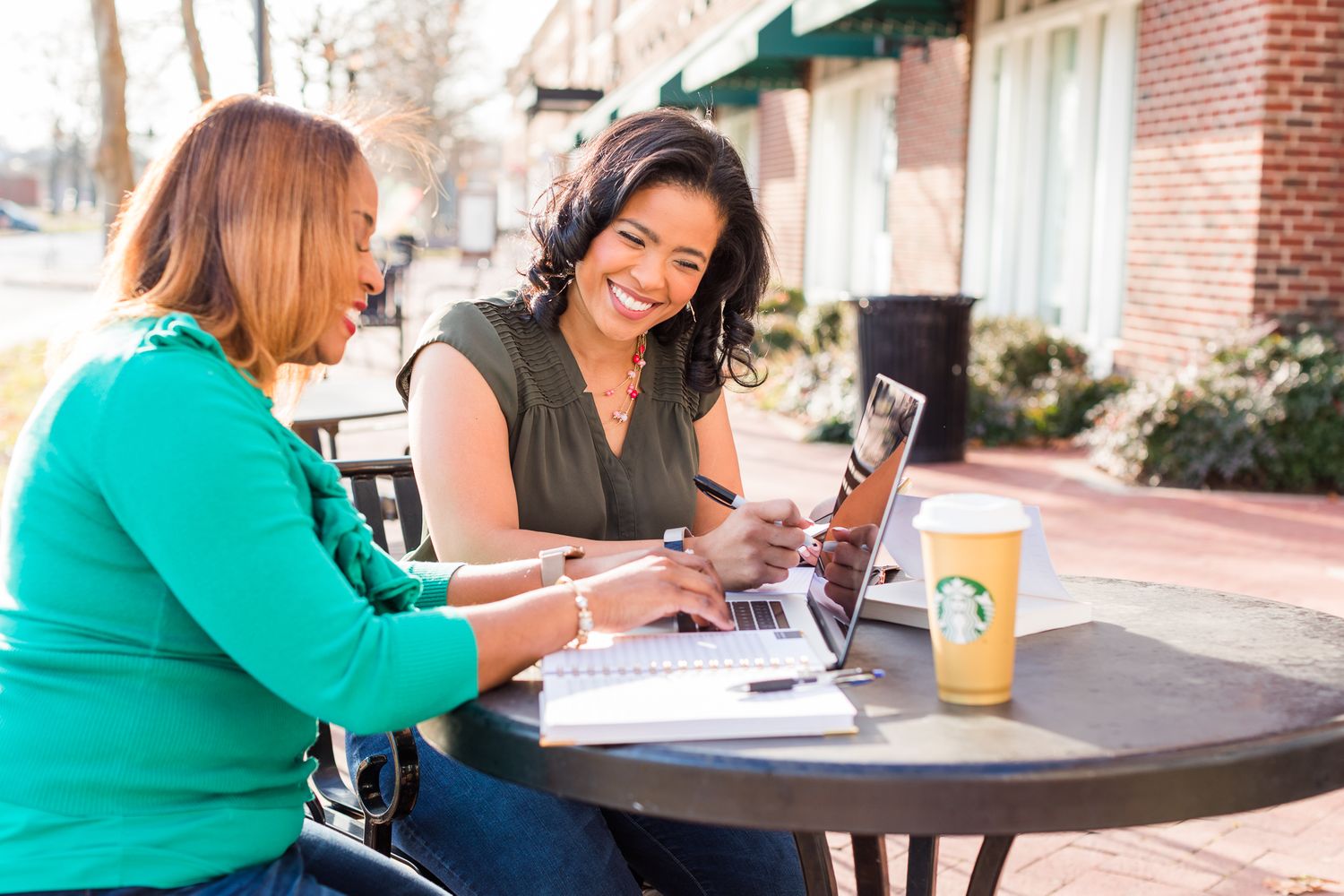 Women working on computer and planning at a cafe table outside