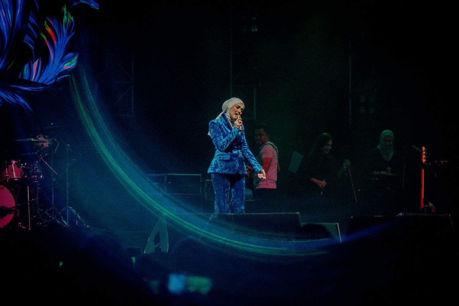 Performer on stage bathed in blue lighting with a curved light effect creating a dramatic atmosphere.
