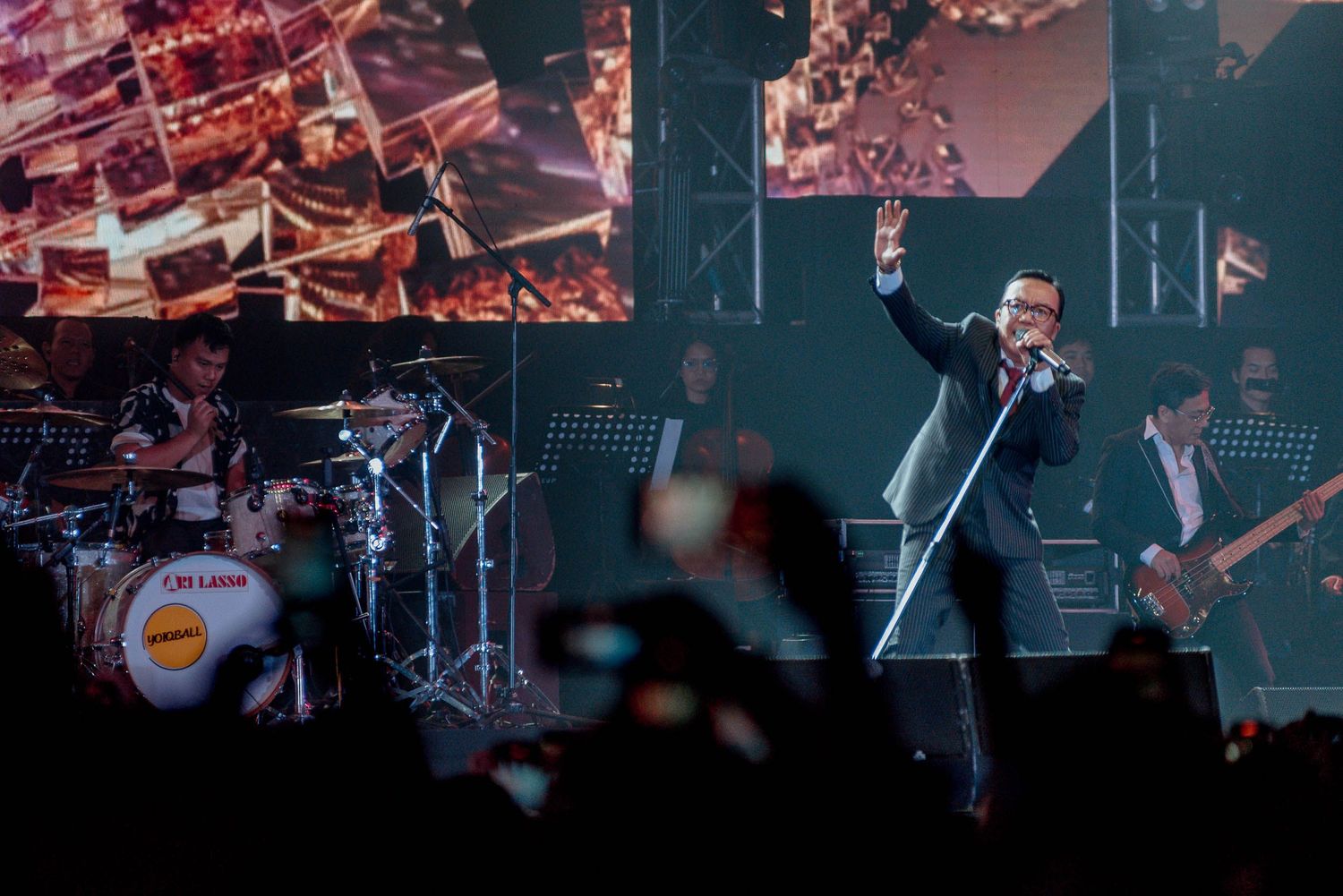 A performer on stage with dramatic lighting and video screens in the background.