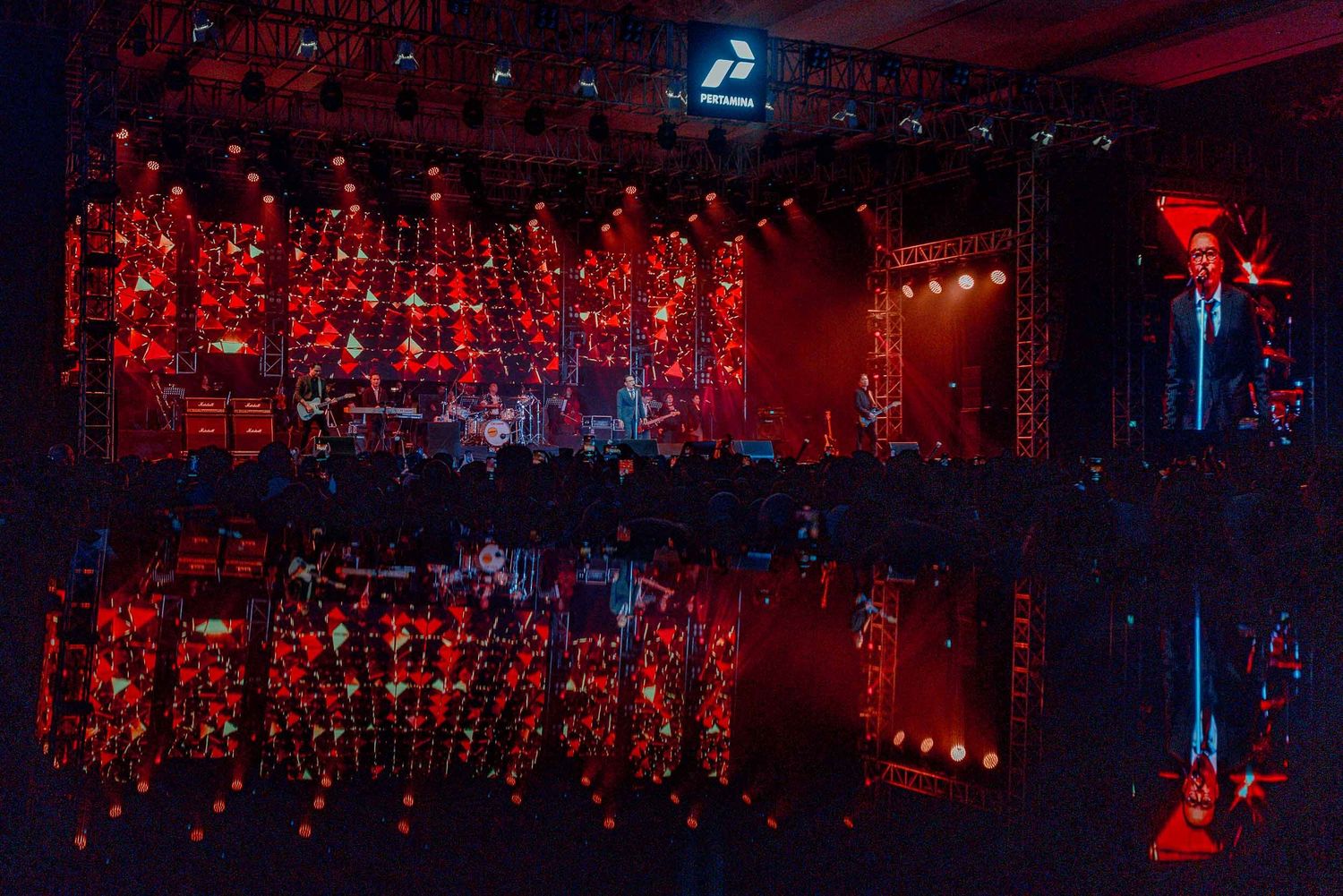 Concert stage with dramatic red lighting and mirror effect creating symmetrical patterns.