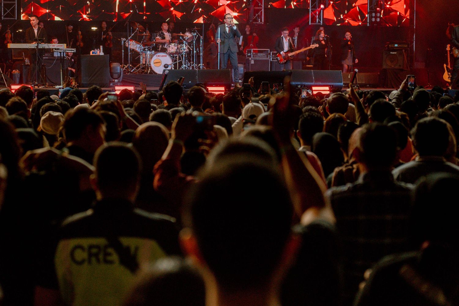Silhouetted crowd watching a live performance with red stage lighting.