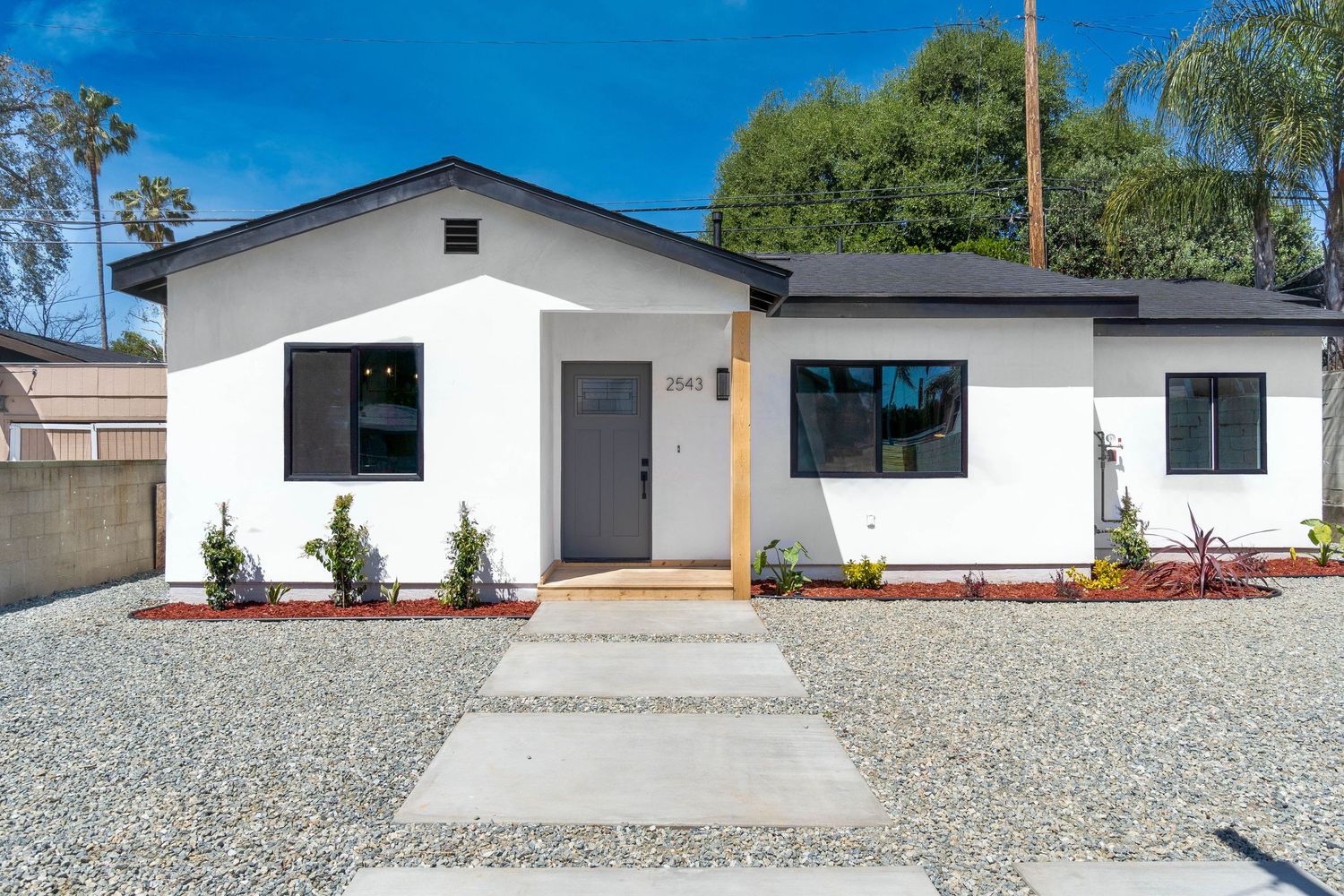 Modern white stucco home exterior with gravel landscaping and concrete walkway.