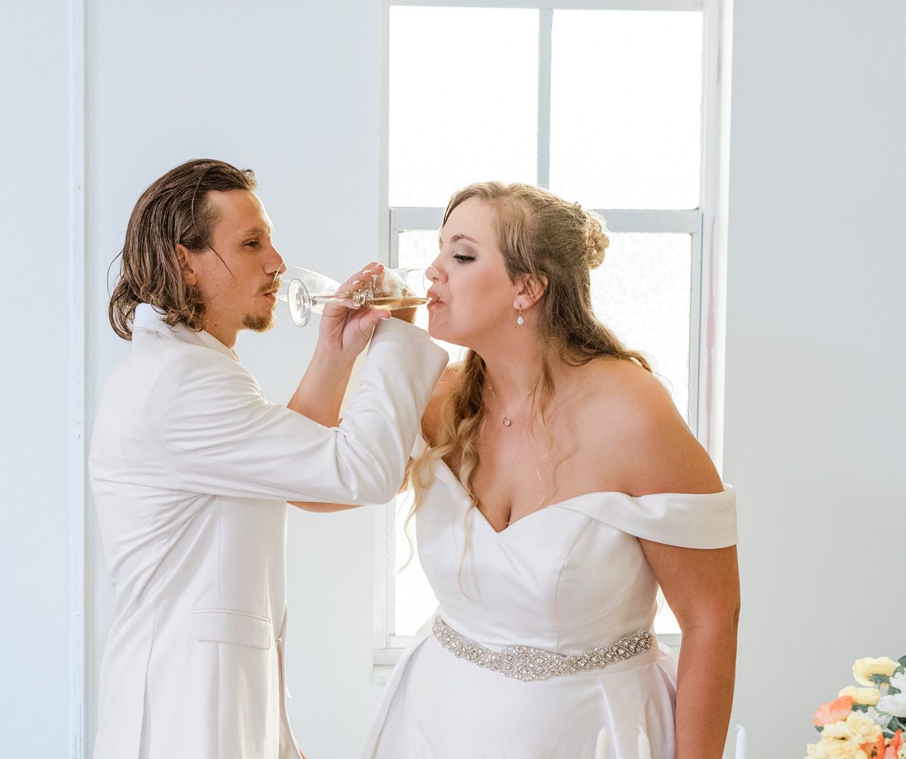 Two people in white outfits share an intimate moment during their wedding celebration.