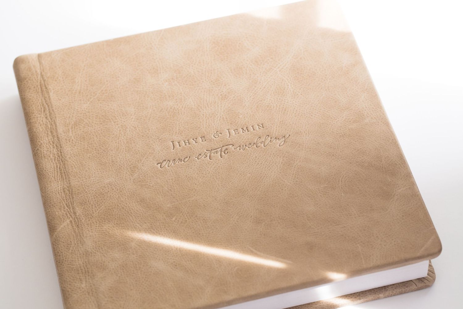 A leather-bound photo album with embossed text on its tan cover sits against a white background.